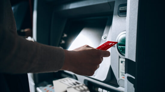 Close up of young woman inserting her bank card into automatic cash machine in the city. Withdrawing money, paying bills, checking account balances, transferring money. Privacy protection, internet and mobile security concept